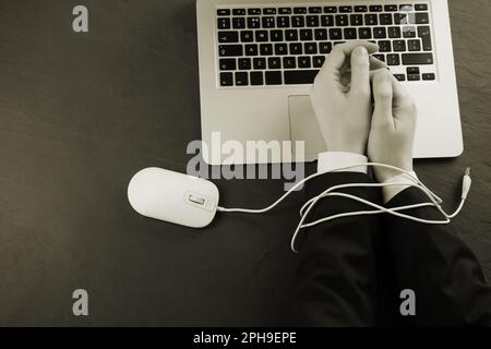 Draufsicht einer Frau mit ihren Händen im Kabel einer Computermaus am schwarzen Tisch, Sepia-Effekt. Internetsucht Stockfoto