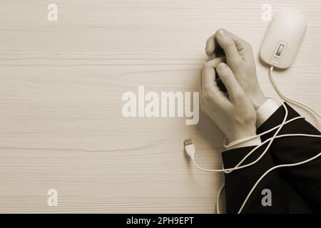 Draufsicht einer Internet-abhängigen Frau mit ihren Händen im Kabel einer Computermaus am Holztisch, Platz für Text. Sepia-Effekt. Stockfoto