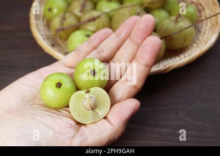 Frische indische Stachelbeeren oder Amla-Querschnitt mit ganzen Früchten in der Hand Stockfoto