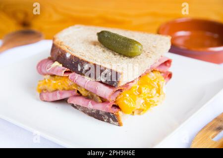 Köstliches amerikanisches Pastrami- und Käsesandwich, dekoriert mit einer Gurke. Stockfoto