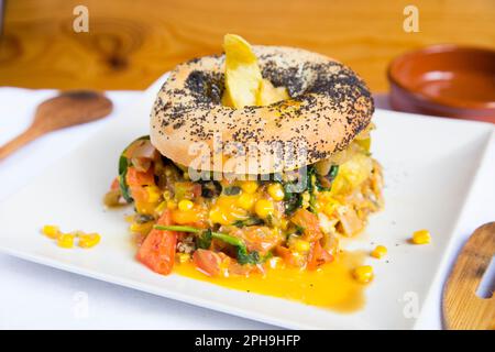 Köstliches Spinat- und Maissandwich auf Bagelbrot. Ein Bagel ist ein Brot, das traditionell aus Weizenmehl hergestellt wird und normalerweise ein Loch in der Mitte hat. Stockfoto