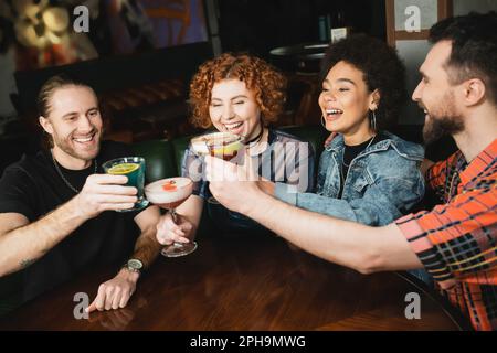 Fröhliche, multiethnische Leute, die abends verschiedene Cocktails in der Bar zuklingeln, Stockbild Stockfoto