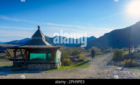 Ein männlicher Tourist geht vorbei an einem runden Pavillon mit einem Pferdekopf auf dem Dach der Rastplätze im Altai-Gebirge Stockfoto