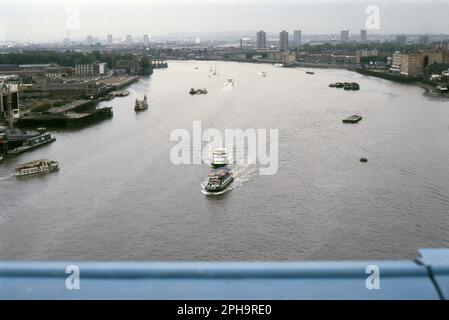 Nach London. 1984. Blick nach Osten vom oberen Fußweg der Tower Bridge über die Themse in London, England. Am rechten Ufer sind Bermondsey und Rotherhithe zu sehen, und auf der linken Seite ist Wapping zu sehen, wie es vor der umfassenden Umgestaltung durch die London Docklands Development Corporation war. Verschiedene Wasserfahrzeuge durchqueren den Fluss. Stockfoto