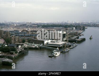 Nach London. 1984. Blick nach Osten vom oberen Fußweg der Tower Bridge über die Themse in London, England. Das Foto zeigt Wapping, wie es vor der umfassenden Sanierung durch die London Docklands Development Corporation war. Im Vordergrund sehen Sie die British & Foreign Wharf und HMS President, eine Einrichtung des Royal Naval Reserve. Stockfoto