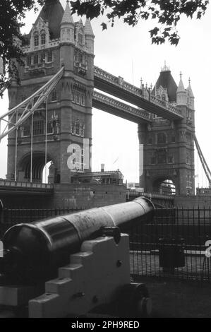 Nach London. 1984. Blick auf die Tower Bridge von Tower Wharf am Nordufer der Themse in London, England. Im Vordergrund befindet sich eine der alten Marinekanonen, die außerhalb des Tower of London ausgestellt wurden. Stockfoto