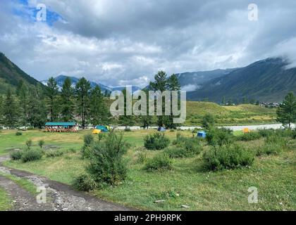 Orte zum Ausruhen mit Hütten und Zelten mit Autos von Touristen in der Nähe des Flusses in Altai Stockfoto