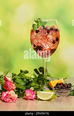 Kalte Sangria mit trockenen Rosenknospen im Weinglas, mit Zutaten auf einem Tisch im Sommer-Hintergrund Stockfoto