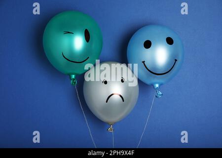 Ballon mit traurigem Gesicht unter glücklichen auf blauem Hintergrund. Depressionskonzept Stockfoto