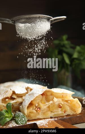 Puderzucker auf köstliche Apfelstrudel-Stücke auf Holzbrett streuen, Nahaufnahme Stockfoto