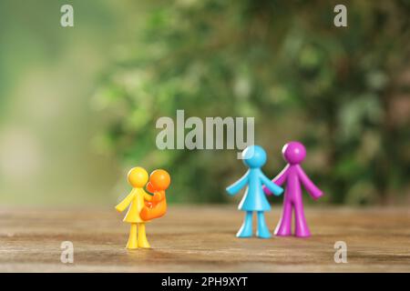 MYKOLAIV, UKRAINE - 04. JANUAR 2022: Bunte menschliche Figuren auf Holztisch vor unscharfem grünen Hintergrund. Leihmutterschaftskonzept Stockfoto