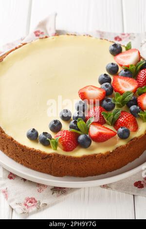 Zarter süßer New Yorker Käsekuchen mit frischen Beeren und Minze aus nächster Nähe auf einem Teller auf dem Tisch. Vertikal Stockfoto