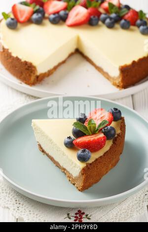 Ein Stück klassischer New Yorker Käsekuchen mit frischen Beeren auf dem Teller auf dem Holztisch. Vertikal Stockfoto