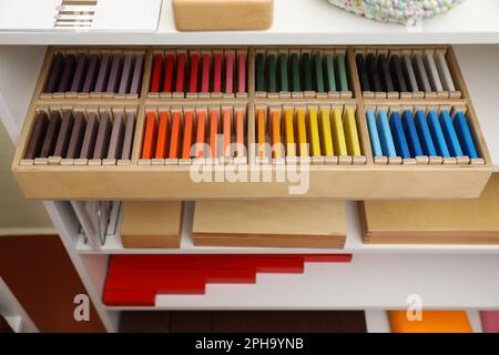 Holzkiste mit Farbtabletten und anderen montessori-Spielzeugen auf Regalen Stockfoto