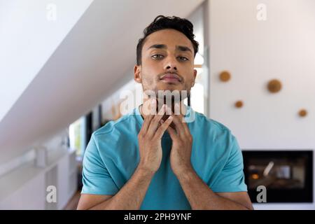 Ein birassistischer Mann, der seinen Hals berührt und in den Badezimmerspiegel schaut Stockfoto