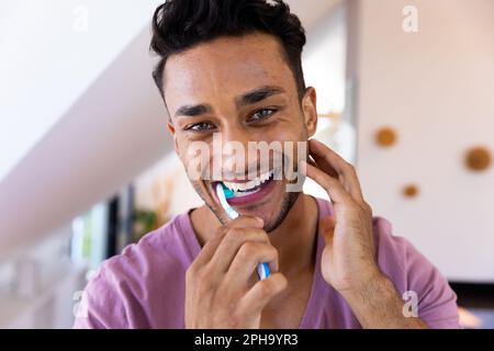 Porträt eines lächelnden birassischen Mannes, der im Badezimmer Zähne putzt Stockfoto