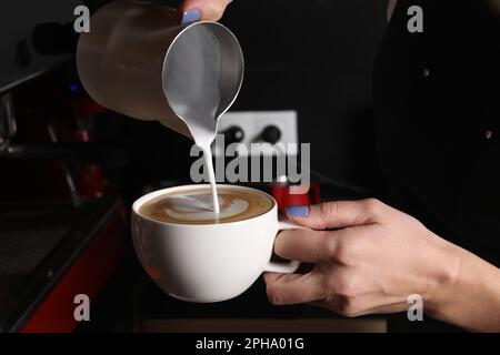 Der Barista gießt aufgeschäumte Milch aus dem Pitcher in eine Tasse aromatischen Kaffees im Café Stockfoto