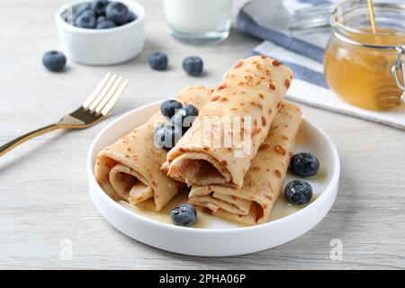 Köstliche Crepes mit Blaubeeren und Honig auf einem weißen Holztisch Stockfoto