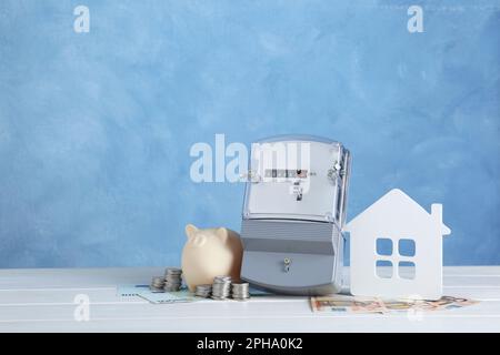 Stromzähler, Sparschwein, Hausmodell und Geld auf weißem Holztisch. Platz für Text Stockfoto