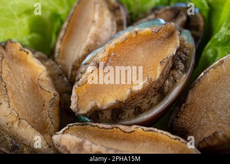 Köstliche rohe Abalone auf einem Teller mit Salat auf Holztisch. Stockfoto