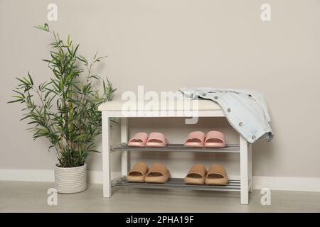 Elegante Aufbewahrungsbank mit verschiedenen Paar Gummipantoffeln und wunderschönen Zimmerpflanzen in der Nähe der weißen Wand im Flur Stockfoto