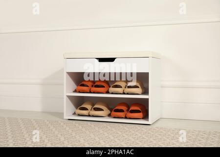 Eleganter Aufbewahrungsschrank mit verschiedenen Paar Gummipantoffeln in der Nähe der weißen Wand im Flur Stockfoto