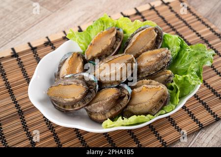 Köstliche rohe Abalone auf einem Teller mit Salat auf Holztisch. Stockfoto