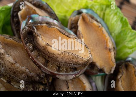 Köstliche rohe Abalone auf einem Teller mit Salat auf Holztisch. Stockfoto