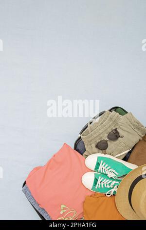 Offener Koffer und Gepäck mit verschiedenen eingepackten Kleidungsstücken. Reisekonzept. Vertikales Foto, Kopierbereich, Draufsicht Stockfoto