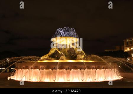 Der Tritons-Brunnen (bei Nacht) ist ein Brunnen, der sich direkt vor dem Stadttor von Valletta, Malta, befindet. Es besteht aus drei Bronze-Tritonen, die ein großes Becken bilden, auf einem konzentrischen Boden aus Beton ausbalanciert und mit Travertinplatten verkleidet sind. Der Brunnen ist eines von Maltas wichtigsten modernistischen Wahrzeichen. Entwickelt und gebaut zwischen 1952 und 1959. Der Busbahnhof und der Bahnhof befinden sich in der Nähe. Stockfoto