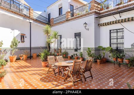 Andalusische Terrasse mit Holztisch und -Stühlen, Wände mit wunderschönen Fliesen und Fußboden mit braunen Porzellanpflastern mit durchgehenden Fliesen