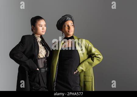 Trendige interrassistische Modelle in Frühlingsbekleidung, die sich posieren und wegschauen, isoliert auf grauem Stockbild Stockfoto