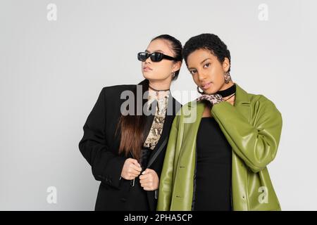 Gut gekleidete interrassistische Modelle in Ledermantel und Jacke, die isoliert auf grauem Stockbild posieren Stockfoto