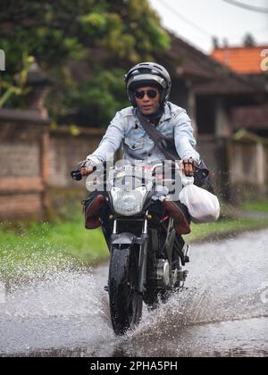 Sidemen, Bali, Indonesien - 24. März 2023: Unidentifizierte Personen pendeln durch eine überflutete Straße. Stockfoto