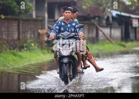 Sidemen, Bali, Indonesien - 24. März 2023: Unidentifizierte Personen pendeln durch eine überflutete Straße. Stockfoto