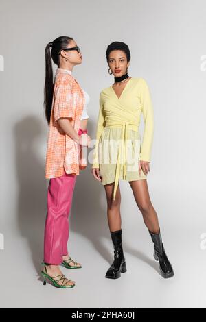 Die ganze Länge voller stylischer Modelle aus verschiedenen Rassen in hellen Frühlingsbekleidung, die auf grauem Hintergrund posieren, Stockbild Stockfoto