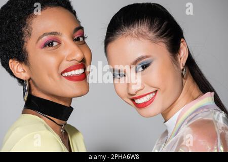 Porträt von hübschen multiethnischen Freunden mit farbenfrohem Visier auf grauem Hintergrund, Stockbild Stockfoto