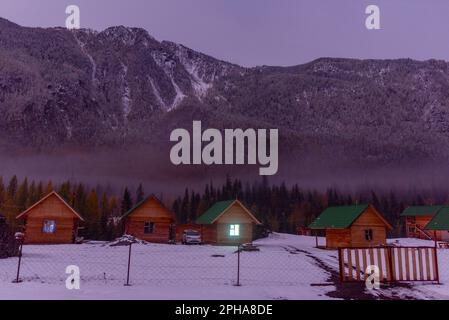 Altai, Russland - 02. Oktober 2022 Ein Honda HRV-Fahrzeug steht neben Ferienhäusern mit einem leuchtenden Fenster in der Nähe eines Waldes unter einem Berg mit Nebel und sn Stockfoto