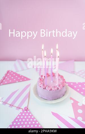 Zarter lavendelrosa Bento-Kuchen auf einem Teller mit pinkem Hintergrund mit Partyflaggen, Kerzen brennen auf dem Kuchen. Feier, alles gute zum Geburtstag Stockfoto