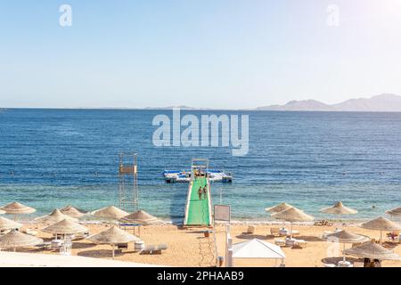 Luxuriöser Strand vor dem Hintergrund der Schönheit des Meeres mit Korallenriffen. Schöner Strand mit Liegen, strohgedeckten Sonnenschirmen und Palmen. Stockfoto