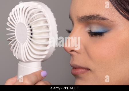 Eine junge Frau erfrischt sich an einem heißen Sommertag mit einem kleinen Handfächer Stockfoto