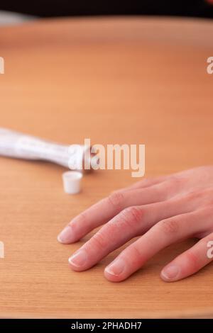 Hochwinkelweicher Fokus der anonymen weiblichen Hand auf einem Holztisch mit offenem Rohr medizinischer Salbe zur Hautpflege Stockfoto