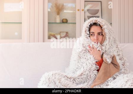 Ermüdete Frau mit roter laufender Nase und kaltem Fieber, die unter einer warmen Decke zittert, während sie sich auf der Couch entspannt Stockfoto