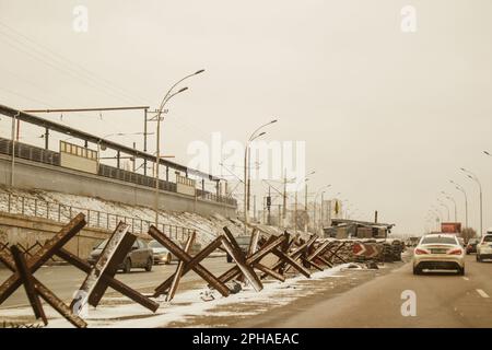 Kiew, Ukraine 2. Februar 2023 Eine Autobahn in einer Militärstadt mit Panzerabwehrbarrieren Igel am Straßenrand. Autos fahren im Winter auf einer Autobahn Stockfoto