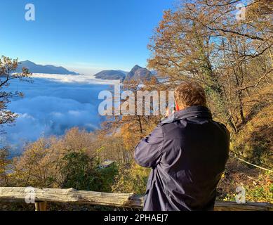 Fotograf, der Fotos auf dem Berggipfel San Salvatore über der Wolkenlandschaft mit Sonnenlicht und klarem Himmel in Lugano, Tessin in der Schweiz macht. Stockfoto