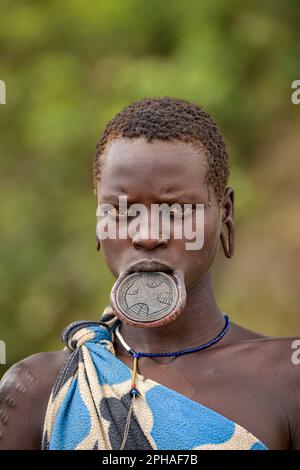 Ein Porträt einer jungen Mursi-Frau mit einer großen Lippenplatte, einer traditionellen Form von Körperdekoration, die äthiopische Frauen tragen Stockfoto