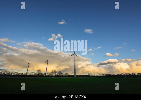 Dichte bunte Regenwolken mit blauem Himmel und eine flache Landschaft mit drei Windmühlen Stockfoto