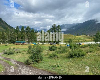 Altai, Russland - 02. Oktober 2022 Freizeitangebote mit einem Pavillon und Zelten mit Touristenautos in der Nähe des Flusses in Altai in der Nähe der Berge. Stockfoto