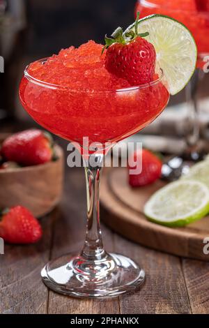 Nahaufnahme von gefrorenem Erdbeerdaiquiri, garniert mit Erdbeeren und Limettenscheiben auf Holzhintergrund Stockfoto