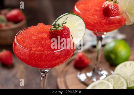 Nahaufnahme von gefrorenem Erdbeerdaiquiri, garniert mit Erdbeeren und Limettenscheiben auf Holzhintergrund Stockfoto